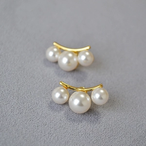 Gros plan de boucles d'oreilles dorées élégantes avec trois perles blanches graduées