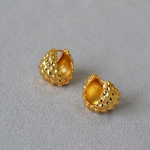 Macro detail of gold-plated spherical earrings featuring a unique faceted texture