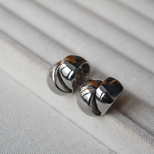 Close-up of polished silver double-C twisted stud earrings on a beige velvet tray