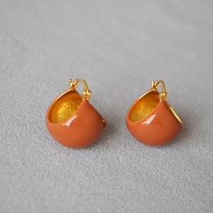 Gros plan de boucles d'oreilles goutte en émail rouge brique et placage doré
