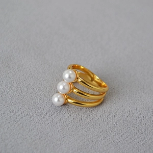 Minimalist multi-layer gold-plated brass ring with three elegant pearls on a grey fabric