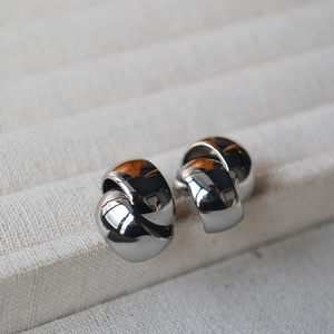 Close-up of polished silver twisted hoop earrings on a beige velvet jewelry display