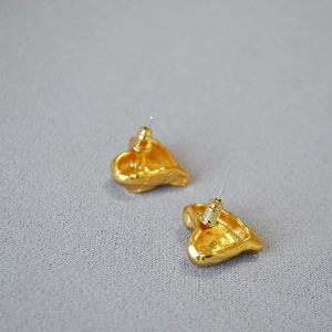 Detail view of gold-plated irregular heart earrings with textured surface and back studs