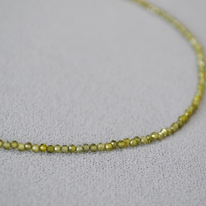 Vue macro de perles facettées en pierre vert olive sur un collier délicat