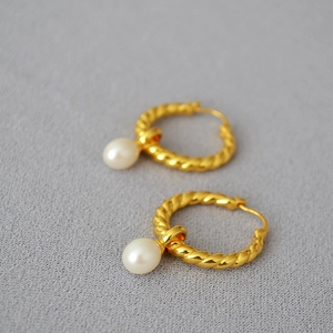 Gros plan de boucles d'oreilles torsadées dorées avec perles d'eau douce sur tissu gris