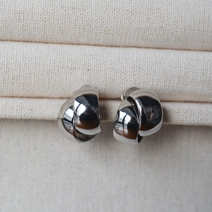 Detailed macro view of silver double-loop twisted knot earrings on beige fabric