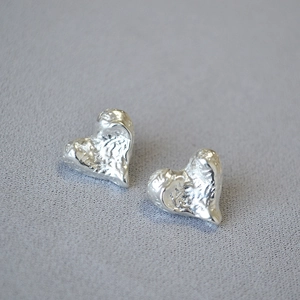 Macro detail of silver heart stud earrings with irregular lava texture and hammered finish