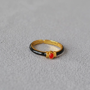 Detailed macro view of an adjustable gold-plated ring featuring black enamel and red stone