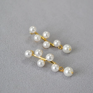 Detail of elegant gold earrings with white pearls arranged in a botanical branch pattern