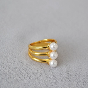 Detail of three-layer gold-plated ring with three white artificial pearls on gray fabric