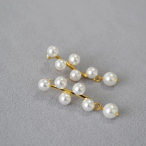 Macro detail of gold twig earrings featuring elegant white pearls on textured grey fabric