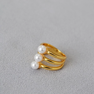 Macro shot of minimalist gold-plated multi-layer ring featuring three inset white pearls