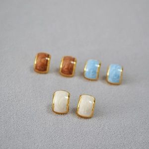 Detailed macro view of U-shaped enamel earrings set in brown, sky blue, and off-white