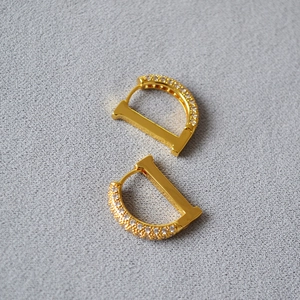 Minimalist D-shaped gold earrings with paved zircon stones shown from a top-down view