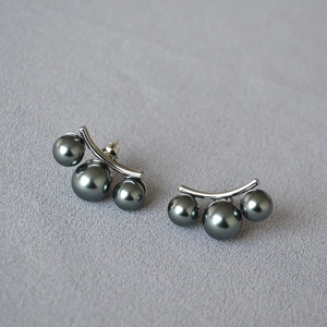 Détail de boucles d'oreilles incurvées argentées avec trois perles gris foncé sur tissu