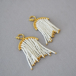 Detail of bohemian white seed bead tassel earrings with golden hardware on a grey surface