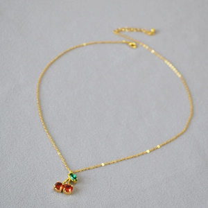 Détail du collier pendentif cerise rouge avec chaîne dorée et feuille verte sertie