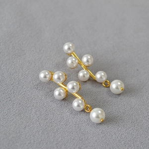 Elegant gold pearl earrings with a geometric fringe design on a textured background