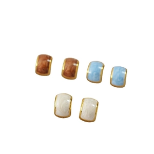 Three pairs of geometric C-shaped enamel earrings in caramel, sky blue, and creamy white