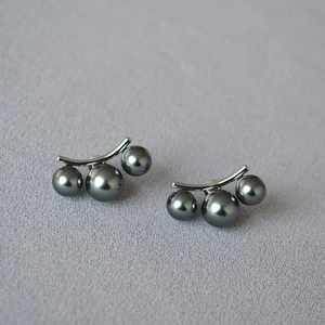 Détail de boucles d'oreilles argentées avec trois perles gris foncé sur tissu violet