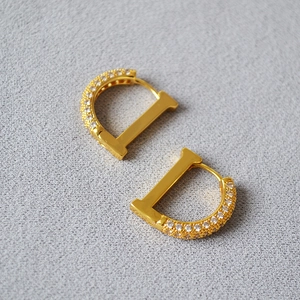 Golden D-shaped huggie earrings with sparkling zircon crystals in a minimalist design