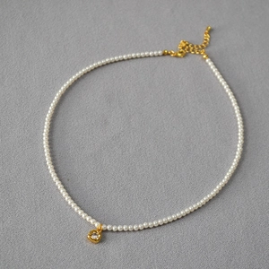 Détail du collier de perles avec pendentif cœur doré, centre en zircon et fermoir mousqueton