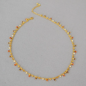 Close-up of golden necklace with colorful beads, lobster clasp, and adjustable chain