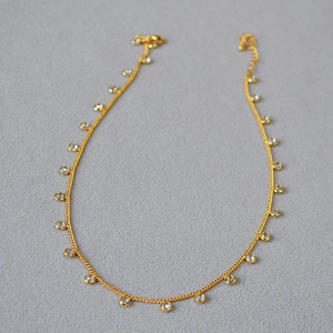 Close-up of a gold-plated necklace with circular crystal pendants on a textured background