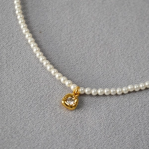 Détail d'un collier de perles avec pendentif carré doré orné d'un zircon étincelant