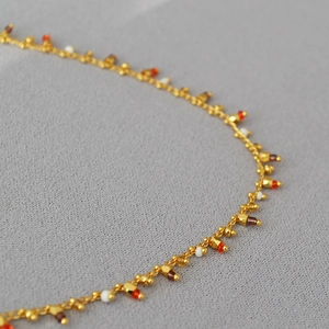 Close-up of minimalist gold chain necklace with colorful orange and white bead accents