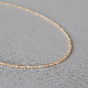 Gros plan d'un collier de perles en zircon champagne de 2mm sur un tissu gris texturé élégant
