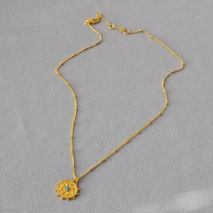 Détail d'un collier pièce dorée vintage avec motifs en relief et incrustation turquoise
