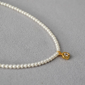 Détail d'un collier de petites perles avec pendentif doré irrégulier et pierre zircon