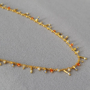 Macro detail of gold beaded fringe necklace with colorful charms on grey fabric