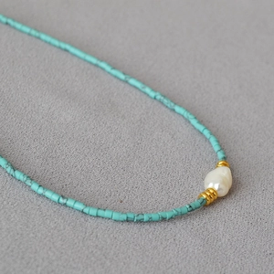 Close-up of a minimalist necklace with turquoise beads and a white baroque pearl