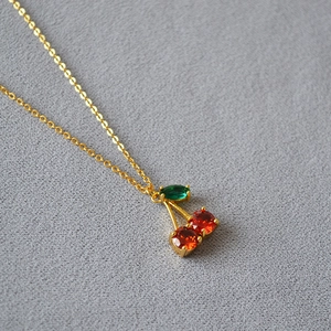 Gros plan du pendentif cerise plaqué or avec cristaux rouges et détail de feuille verte