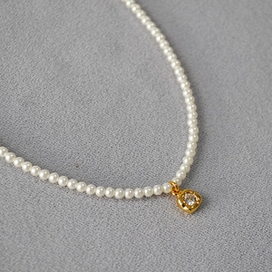 Vue macro d'un collier de perles avec un pendentif floral carré doré et zircon