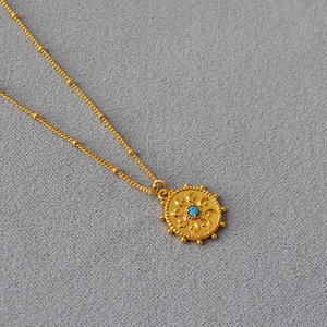 Détail du collier doré avec pendentif soleil rayonnant et turquoise sur chaîne à billes