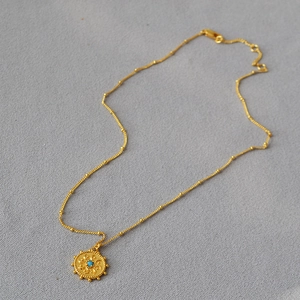 Détail du collier pièce soleil dorée avec incrustation turquoise et chaîne à billes