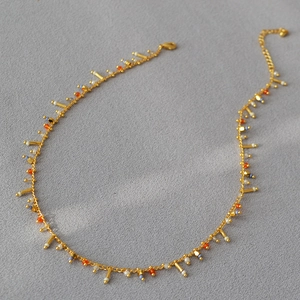 Close-up of gold chain necklace with colorful beads and geometric charms on grey texture