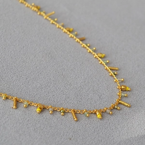 Detail of delicate gold chain necklace with yellow beads and bohemian tassels
