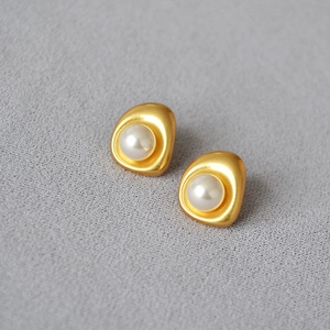 Detail of baroque pearl earrings with matte gold plating on a soft grey fabric surface
