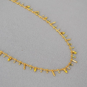 Detail of gold chain with yellow and green beads and dangling bar tassel charms