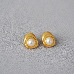 Detail of baroque gold-plated brass stud earrings with a matte texture and white pearl center