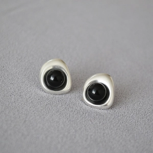 Detail of silver irregular metal stud earrings featuring a glossy black round gemstone center