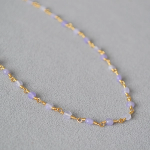 Macro detail of wire-wrapped lavender beads on a gold-plated brass necklace chain