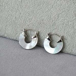 Détail de boucles d'oreilles argentées en U avec incrustation de nacre blanche irisée