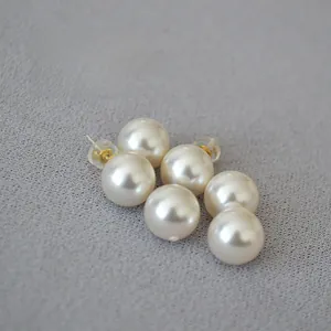 Close-up of minimalist white crystal pearl earrings with gold needles on grey fabric