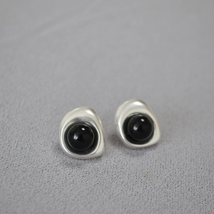 Macro shot of silver baroque stud earrings with black sphere stone inlay on grey fabric