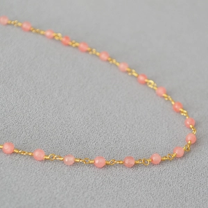 Détail macro du collier artisanal avec pierres roses et fils dorés enroulés